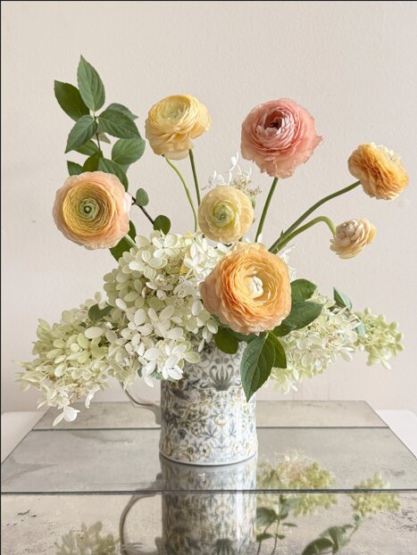 Peach and yellow ranunculus arrangement with hydrangea in a patterned pitcher